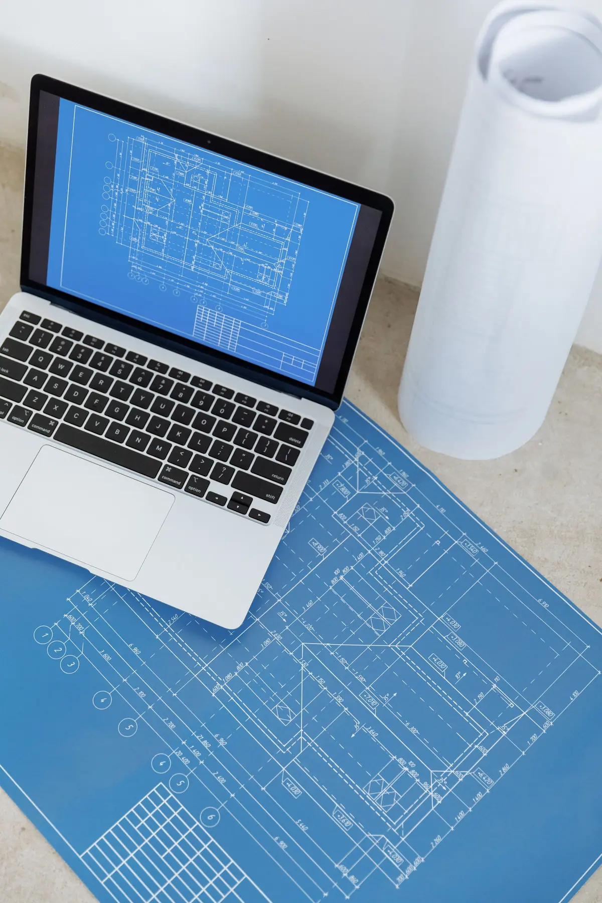 Building plans open on a laptop beside rolled-up blueprints